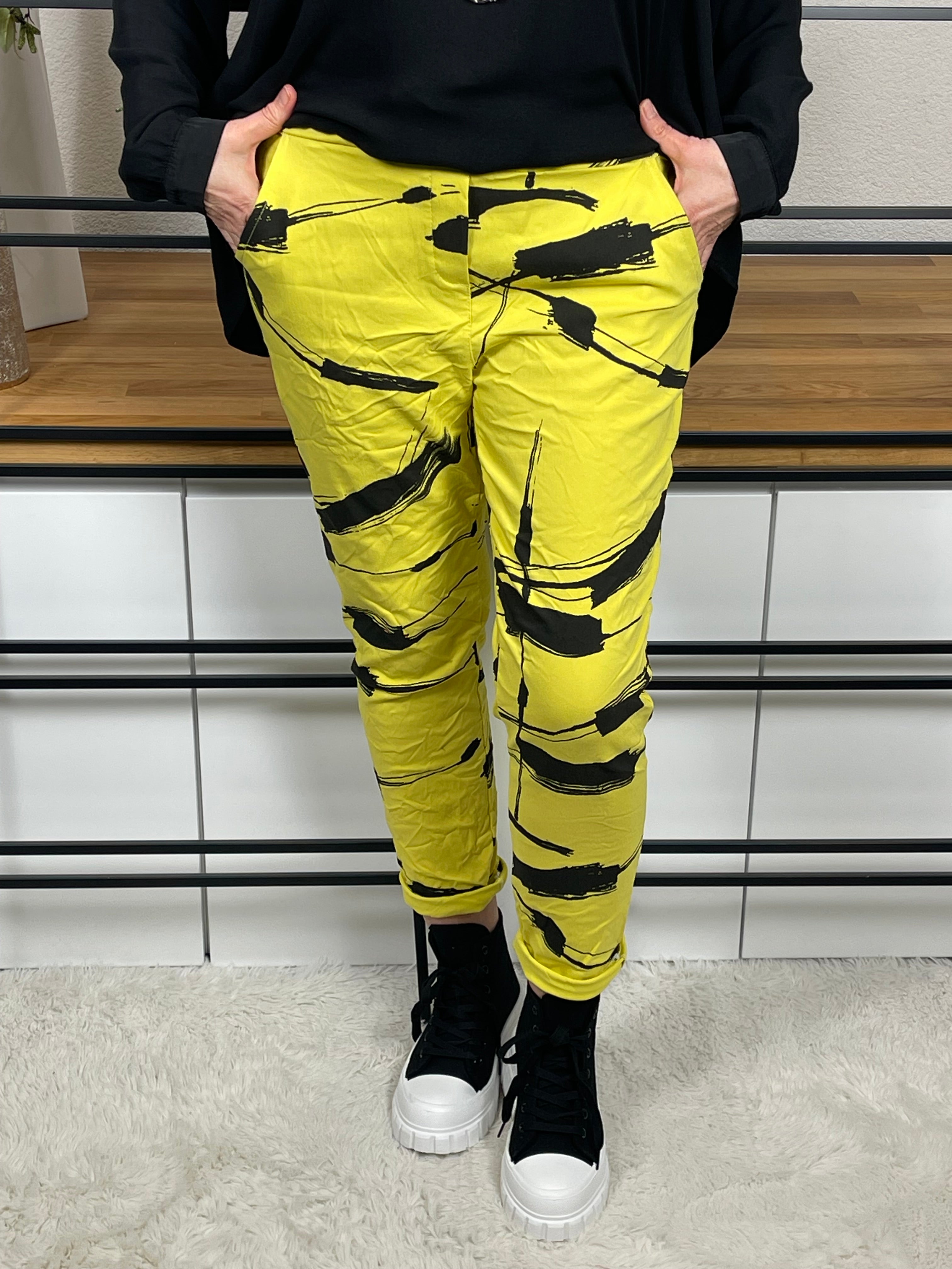 Nahansicht von vorne einer Damen - Jogpant in Gelb mit schwarzem Brushstroke-Print, angewinkeltem Bein, kombiniert mit trendigen High - Sneakern in schwarz. Perfekter Streetstyle - Look für Freizeit und Alltag.