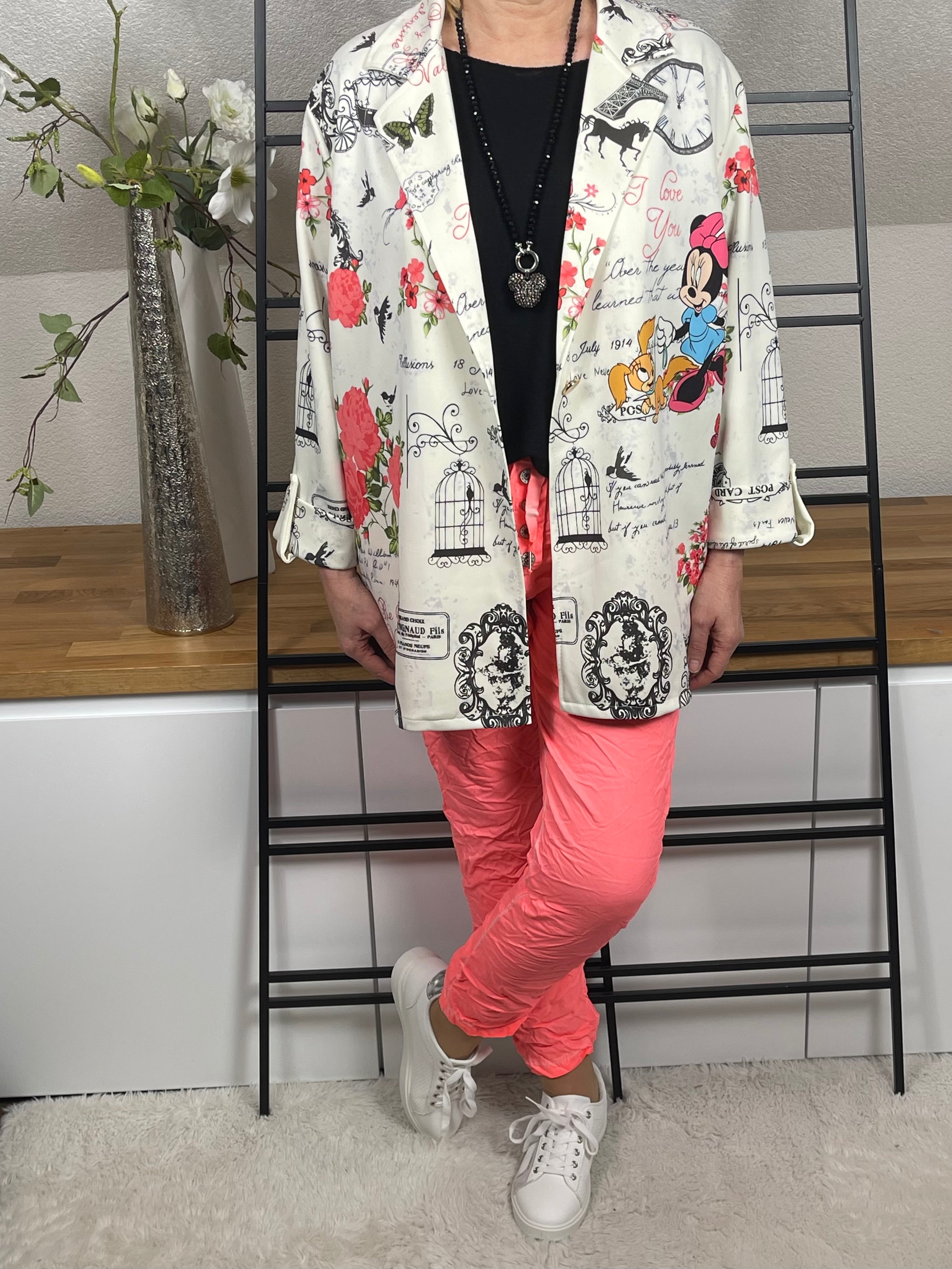 Mickey - Mouse Blazer in Weiß-Bunt, offen getragen mit einem schwarzen Strick-Basic, kombiniert mit einer neon-korallfarbenen Jogpant, Vario Kette mit Mickey - Anhänger und weiß-silbernen Sneakern. Moderner und lässiger Look.